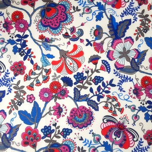 Könnte beinhalten: Ein weißer Stoff mit einem sich wiederholenden Muster aus blauen, roten und pinkfarbenen Blumen. Die Blumen sind stilisiert und haben einen verspielten Charakter. Der Hintergrund ist hellcremefarben.