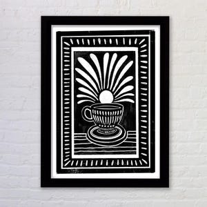 Puede incluir: Ilustración en blanco y negro de una taza de té y un platillo con un sol estilizado que sale detrás. La imagen está enmarcada en un marco negro.