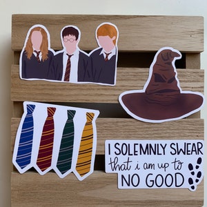 May include: A collection of four vinyl stickers featuring a trio of students in school uniforms, a brown sorting hat, four striped neckties in blue, red, green, and yellow, and a white rectangular sticker with the text I SOLEMNLY SWEAR that i am up to NO GOOD.
