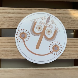 Puede incluir: Una pegatina circular con un diseño gráfico estilizado que presenta una forma geométrica central en color tostado y gris que recuerda a una lámpara o paraguas, flanqueada por dos líneas finas y curvas que terminan en motivos florales.