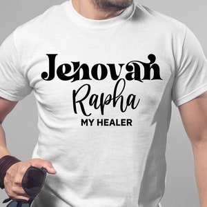 Puede incluir: Camiseta blanca con las palabras "Jehovah Rapha MY HEALER" en escritura negra. La camiseta es lisa y tiene mangas cortas. La persona de la imagen sostiene gafas de sol.