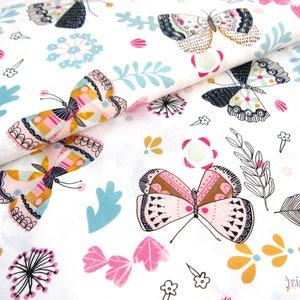 Könnte beinhalten: Weißer Stoff mit einem sich wiederholenden Muster aus bunten Schmetterlingen, Blumen und Blättern. Die Schmetterlinge haben rosa, orange und braune Flügel mit schwarzen Umrissen. Die Blumen sind rosa, gelb und blau. Die Blätter sind grün und braun.