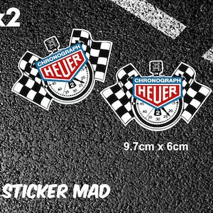 Puede incluir: Dos banderas de carreras a cuadros blanco y negro con un cronómetro Heuer rojo en el centro. El cronómetro tiene una esfera blanca con números y manecillas negros. El texto "CHRONOGRAPH HEUER" está impreso en blanco sobre fondo rojo. El texto "x2" está impreso en negro sobre fondo blanco. El texto "9,7 cm x 6 cm" está impreso en negro sobre fondo blanco. El texto "STICKER MAD" está impreso en blanco sobre fondo negro.