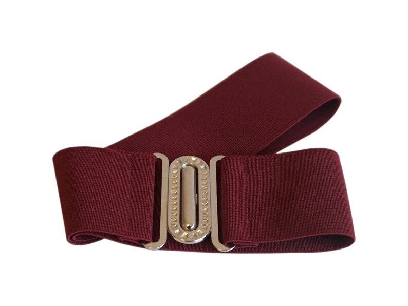 May include: A burgundy elastic belt with a silver-colored buckle. The belt is wide and has a textured appearance. The buckle is rectangular with a decorative design.