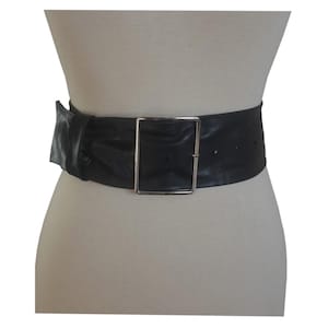 May include: A wide black leather belt with a silver square buckle. The belt is thick and has a slightly textured surface.