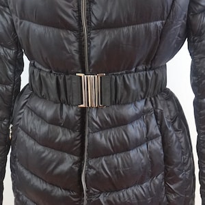 Può includere: Una giacca imbottita nera con cintura e fibbia argentata.