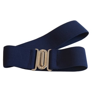 May include: A navy blue elastic belt with a silver-colored buckle. The buckle has a rectangular shape with a decorative design. The belt is shown against a white background.