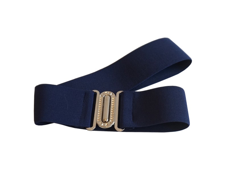 May include: A navy blue elastic belt with a silver-colored buckle. The buckle has a rectangular shape with a decorative design. The belt is shown against a white background.
