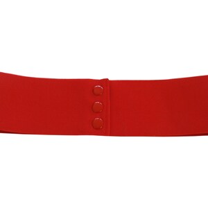 May include: A red elastic belt with four plastic buttons. The belt is made of a stretchy material and is designed to be worn around the waist.
