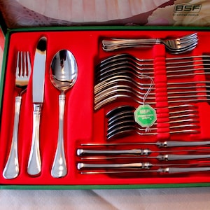 Può includere: Un set completo di posate in acciaio inossidabile in una scatola di presentazione verde e rossa. Il set include forchette, coltelli e cucchiai, ben disposti. La scatola ha un motivo floreale sul coperchio e un'etichetta del marchio.