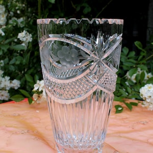 Könnte beinhalten: Eine klare Glasvase mit geschliffenem Kristallmuster. Die Vase hat einen gewellten Rand und einen breiten Boden. Sie ist mit einem Blumenmuster verziert.