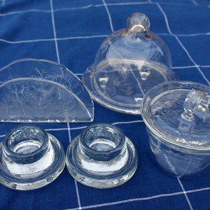 Puede incluir: Un juego de cinco piezas de servicio de vidrio transparente, que incluye una campana, un plato con tapa, un porta servilletas y dos candelabros. Las piezas son todas de vidrio transparente y tienen un diseño simple y elegante.