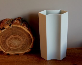 Può includere: Vaso in ceramica bianca con un design geometrico ondulato. Il vaso ha una superficie testurizzata ed è appoggiato su una superficie in legno.