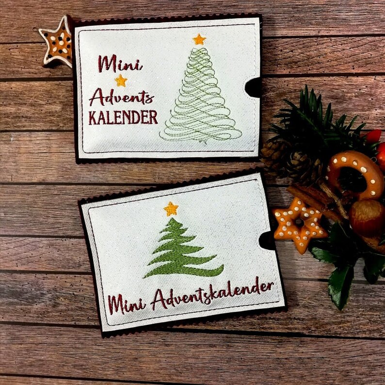 May include: Two white felt Christmas advent calendar pouches with embroidered green Christmas trees and the text "Mini Advent Kalender" and "Mini Adventskalender".
