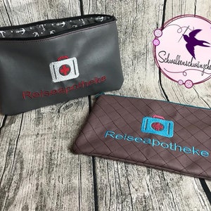 以下が含まれることがあります： 「Reiseapotheke」と刺繍されたジッパー付きポーチが2つ。1つはグレーで白い救急箱のアイコン、もう1つはブラウンで青い救急箱のアイコンが付いています。