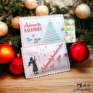 May include: Two white felt pouches with embroidered Christmas designs. The top pouch has a green Christmas tree and the text "Advent Kalender to go". The bottom pouch has a silhouette of an angel and the text "Adventskalender to go".