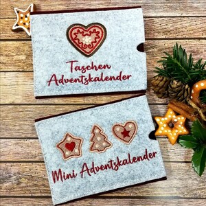 May include: Two gray felt advent calendars with red embroidery. The larger calendar says "Taschen Adventskalender" and features a gingerbread heart. The smaller calendar says "Mini Adventskalender" and features a gingerbread heart, star, and Christmas tree.