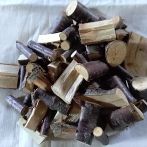 Peut inclure: Un tas de bois de chauffage, composé de morceaux de bois de différentes tailles et formes. Le bois présente un mélange de couleurs brun clair et brun foncé, avec de l'écorce et des extrémités coupées visibles. Les morceaux sont disposés sur une surface claire.