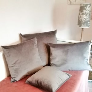 Könnte beinhalten: Vier graue Samt-Kissen auf einem rosa Sofa. Die Kissen sind alle in der gleichen Farbe und Textur, aber in verschiedenen Größen.