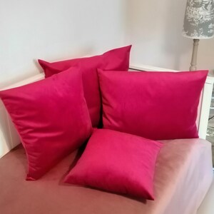 Könnte beinhalten: Vier leuchtend rosa Kissen auf einem rosafarbenen Bettbezug. Die Kissen sind alle gleich groß und gleich geformt und in einem versetzten Muster angeordnet.