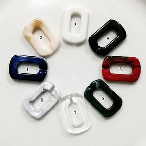 May include: Eight different colored plastic chain links, each with a number from 1 to 8. The links are all rectangular and have a hole in the center. The links are arranged in a circle on a white surface.