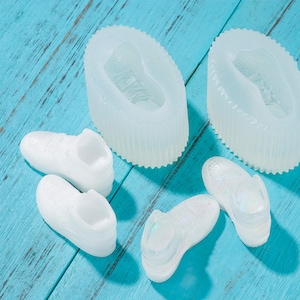May include: Two white silicone moulds for making miniature trainers. The moulds are oval-shaped and have a raised texture. Four miniature white trainers are also shown.
