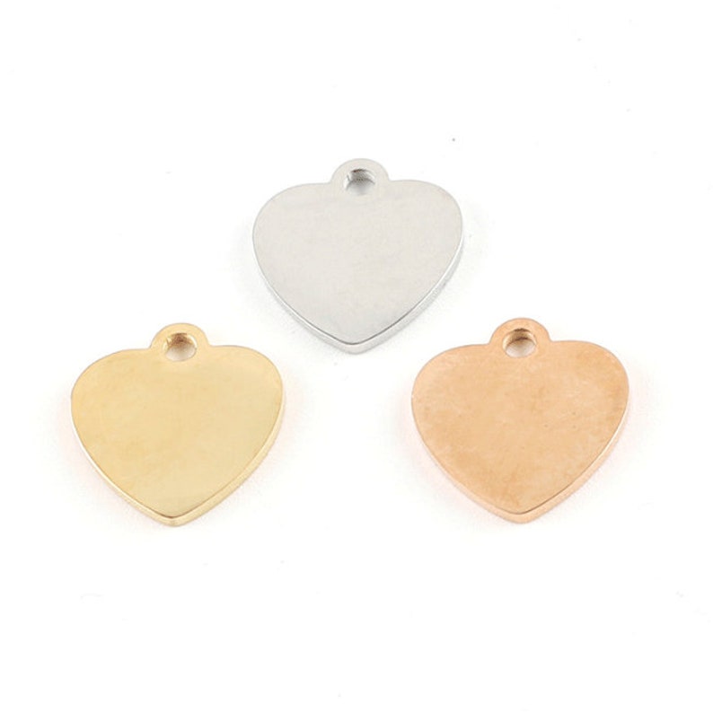 May include: Three heart-shaped metal charms in silver, gold, and rose gold. Each charm has a small loop at the top for attaching to a necklace or bracelet.