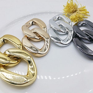 May include: Four metal chain links in different finishes: gold, silver, rose gold, and black. The links are all the same size and shape, and they are arranged in a row.