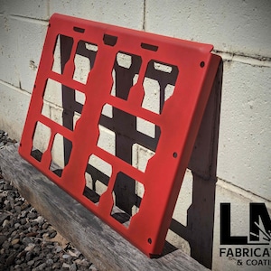 May include: A red metal panel with a grid of rectangular cutouts. The panel is leaning against a white brick wall. The text "LM FABRICATION & COATING" is visible in the lower right corner of the image.
