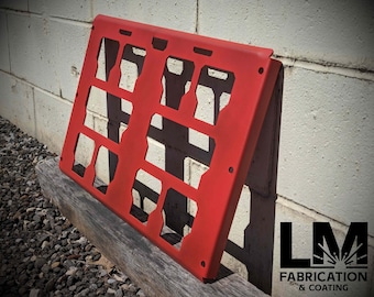 May include: A bright red metal panel with rectangular cutouts, leaning against a concrete wall. The panel is resting on a weathered wooden beam. The logo "LM Fabrication & Coating" is visible in the lower right corner.