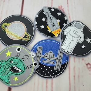 Könnte beinhalten: Fünf gestickte Bügelbilder mit Weltraummotiven. Die Patches sind rund und zeigen eine Rakete, einen Astronauten, eine Raumstation, einen Planeten und einen Außerirdischen.