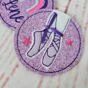 Könnte beinhalten: Kreisförmige, glitzernde lila Aufnäher mit gestickten Ballettdesigns. Ein Aufnäher zeigt Ballettschuhe mit lila Schleife, der andere das Wort "Love". Rosa Sterne ergänzen das Design.