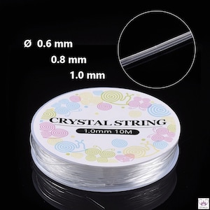 Könnte beinhalten: Eine Spule mit klarem elastischem Faden zum Schmuck basteln. Das Etikett lautet "Crystal String 1.0mm 10M".