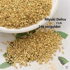 May include: A close-up of a pile of small, gold-colored beads. The beads are round and have a smooth, shiny finish. The text "Miyuki Delica 11/0 24k vergoldet" is visible in the image.