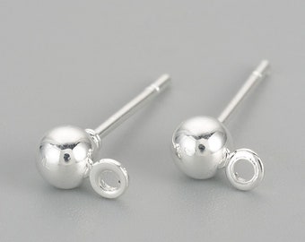 Puede incluir: Dos postes de pendientes de plata con una pequeña bola redonda en la parte superior y un anillo de salto unido a la bola.