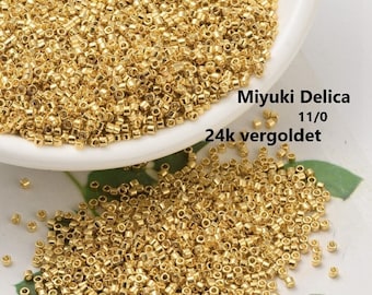 Puede incluir: Primer plano de un montón de pequeñas cuentas doradas. Las cuentas son redondas y tienen un acabado liso y brillante. El texto "Miyuki Delica 11/0 24k vergoldet" es visible en la imagen.