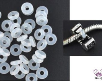 May include: A close-up of a pile of white silicone spacer beads for jewelry making. The beads are small and round with a hole in the center. The beads are used to separate charms on a bracelet or necklace.