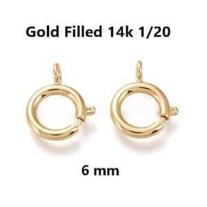 Könnte beinhalten: Zwei goldgefüllte 14k 1/20 Federringverschlüsse. Jeder Verschluss ist ein kreisförmiger Ring mit einem kleinen Hebel zum Öffnen und Schließen. Die Verschlüsse sind 6 mm groß. Der Text auf dem Bild lautet "Gold Filled 14k 1/20" und "6 mm".