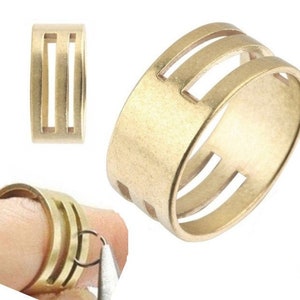 Könnte beinhalten: Goldener Metallring mit drei horizontalen Schlitzen. Der Ring ist so konzipiert, dass er Kabel oder Drähte an Ort und Stelle hält.