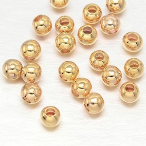 Könnte beinhalten: Eine Sammlung von 20 goldfarbenen runden Perlen mit einem Loch in der Mitte. Die Perlen sind auf einer weißen Oberfläche verstreut.