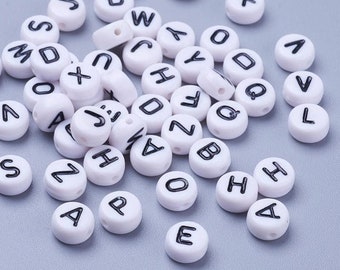 May include: White plastic alphabet beads with black lettering. The beads are scattered on a gray surface.