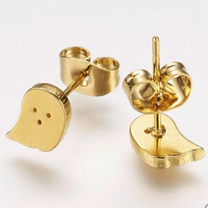 Könnte beinhalten: Ein Paar goldfarbene Ohrstecker. Jeder Ohrring hat ein geisterförmiges Design mit drei kleinen Punktdetails. Die Ohrringe haben einen Stecker und einen Schmetterlingsverschluss. Die Ohrringe befinden sich auf weißem Hintergrund.