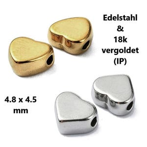 Könnte beinhalten: Herzförmige Perlen in Gold- und Silbertönen. Die goldenen Perlen sind 18 Karat vergoldet. Die Abmessungen betragen 4,8 x 4,5 mm. Der Text auf dem Bild lautet "Edelstahl & 18k vergoldet (IP)".