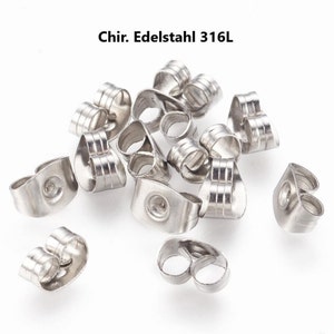 May include: A collection of shiny, silver-colored earring backs. The backs are made of stainless steel and have a butterfly shape. The text "Chir. Edelstahl 316L" is visible in the image.
