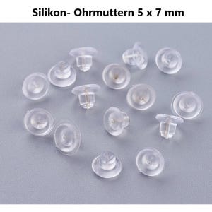 Puede incluir: Un conjunto de topes de pendientes de silicona transparente, de aproximadamente 5 x 7 mm, sobre una superficie gris claro. Los topes de pendientes translúcidos tienen forma de hongo, diseñados para asegurar los pendientes.