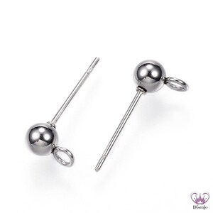 Könnte beinhalten: Zwei silberne Ohrstecker mit einer kleinen Schlaufe am Ende jedes Steckers. Die Stecker haben eine runde Kugel oben.