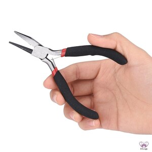 Puede incluir: Un par de alicates de joyer&iacute;a plateados con mangos de goma negra y detalles rojos. Los alicates se sostienen en una mano.