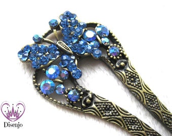 Puede incluir: Una horquilla para el pelo con forma de mariposa adornada con joyas azules. La horquilla es de metal y tiene un acabado marrón oscuro.