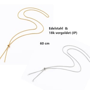 Könnte beinhalten: Zwei verstellbare Halsketten, eine gold und eine silber, mit einem verschiebbaren Knotenschluss. Die goldene Halskette ist aus 18 Karat vergoldetem Edelstahl und 60 cm lang. Die silberne Halskette ist aus Edelstahl.