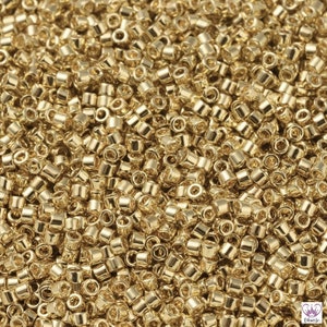 May include: A close-up view of a large quantity of small, gold-colored seed beads. The beads are round and have a smooth, shiny finish.